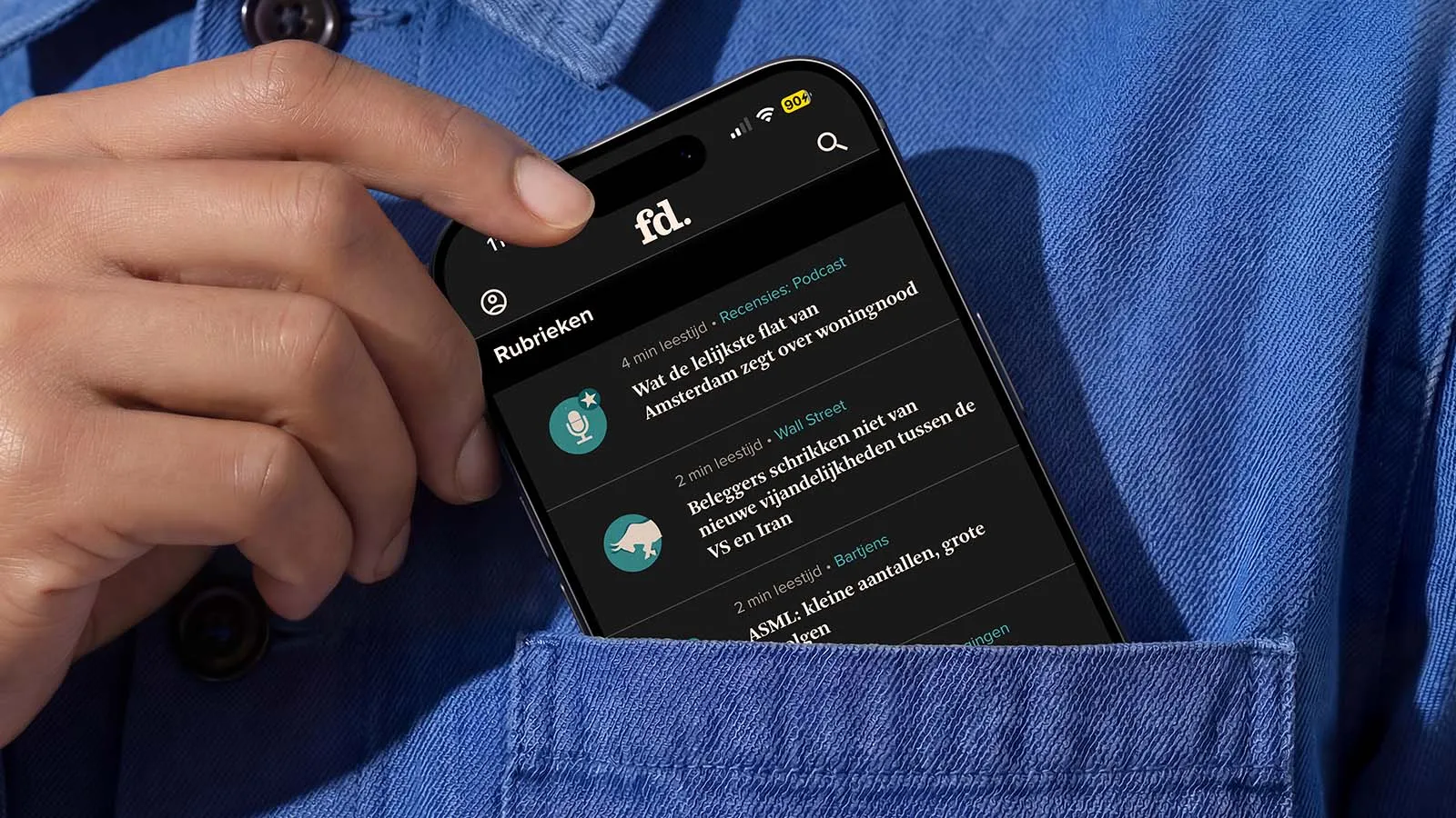 A mobile phone displaying the Het Financieele Dagblad app peeks out of the top pocket of a blue shirt.