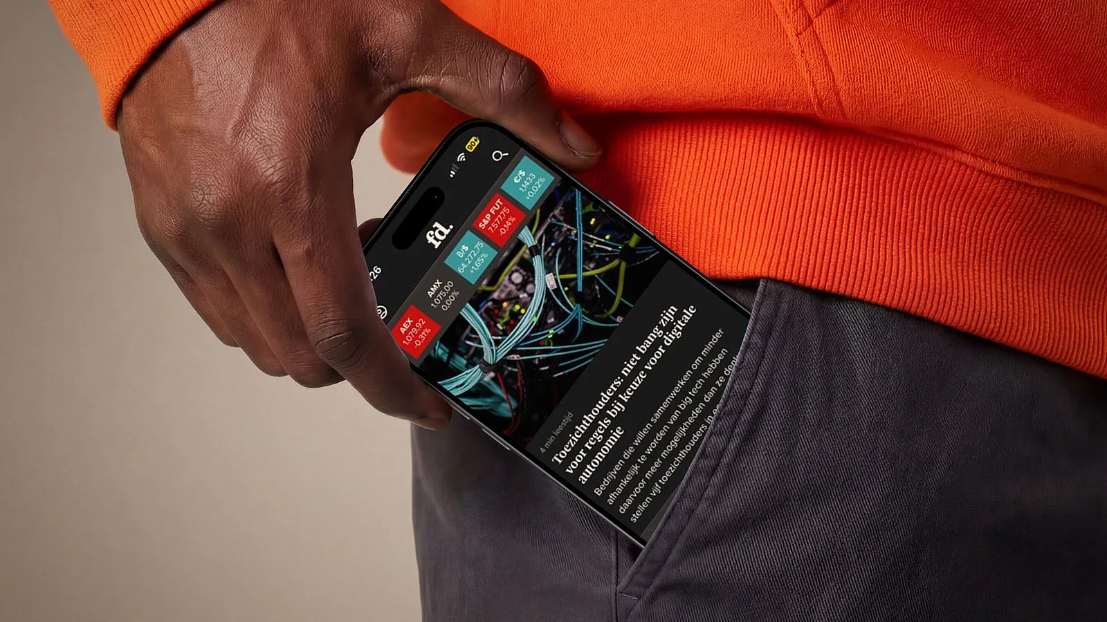 A mobile phone displaying the Het Financieele Dagblad app peeks out of the pocket of pair of jeans.