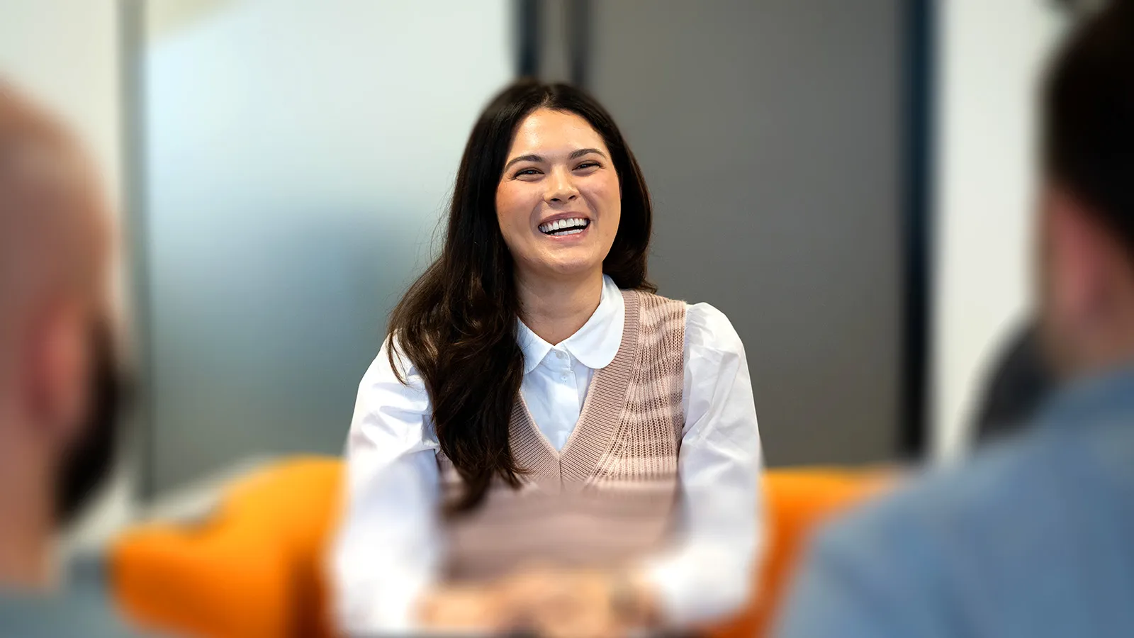 A woman with long, dark hair, wearing a white shirt and pink tank top, smiles warmly at the camera.