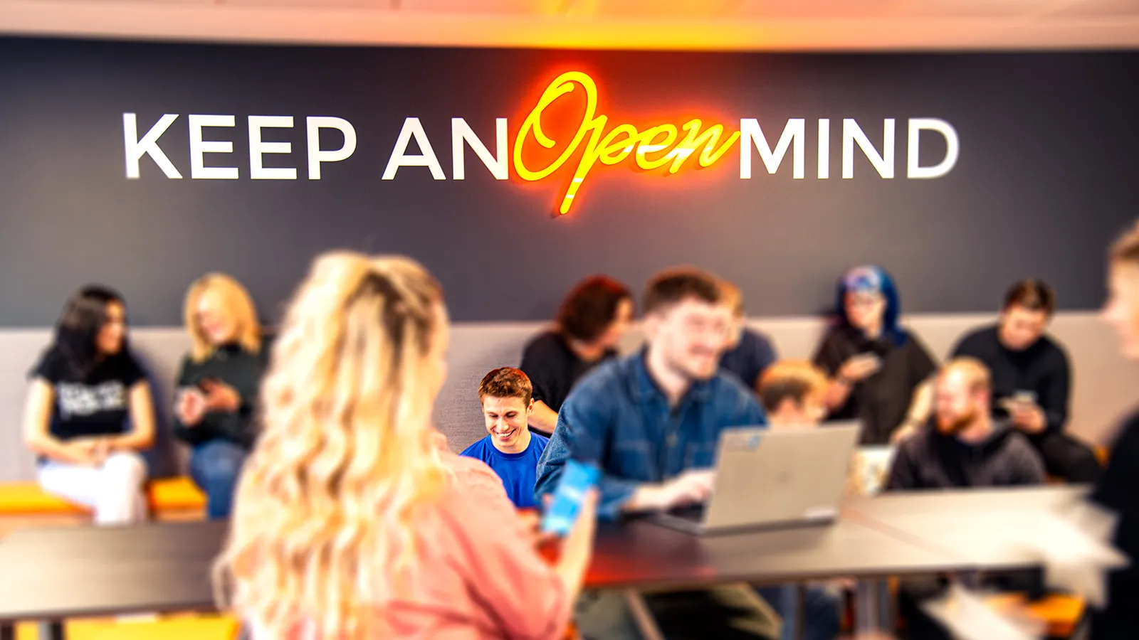 A group of people sit chatting and smiling in front of a sign that says Keep an Open Mind.