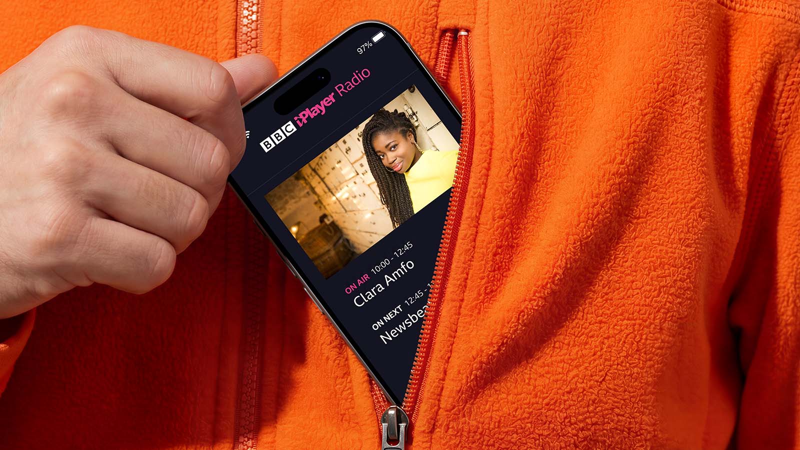 A phone displaying the BBC iPlayer Radio app peeks out of the pocket of an orange shirt.