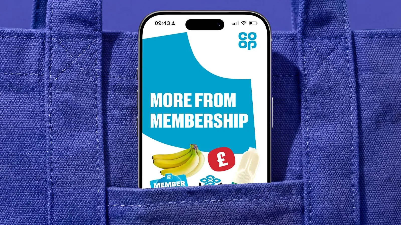 An iPhone displaying the Co-op app peeks out of a blue shopping bag.