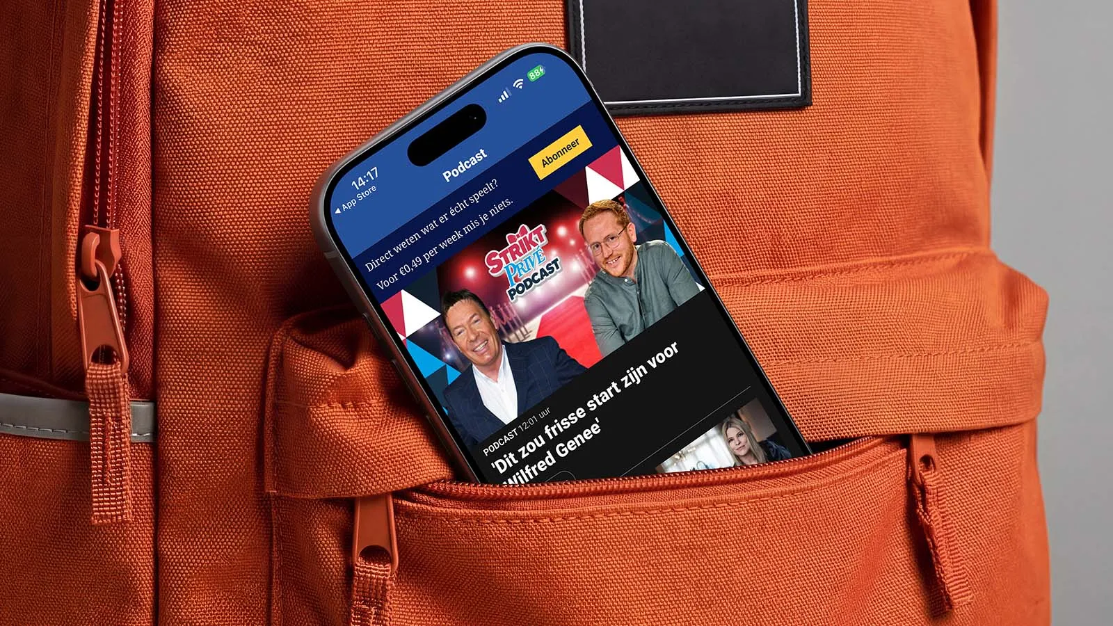 A phone displaying the De Telegraaf news app peeks out of the top pocket of an orange shirt.