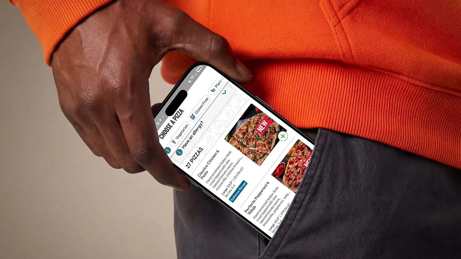 An iPhone 17 peeks out of a man's trouser pocket, displaying the Domino's pizza selector.