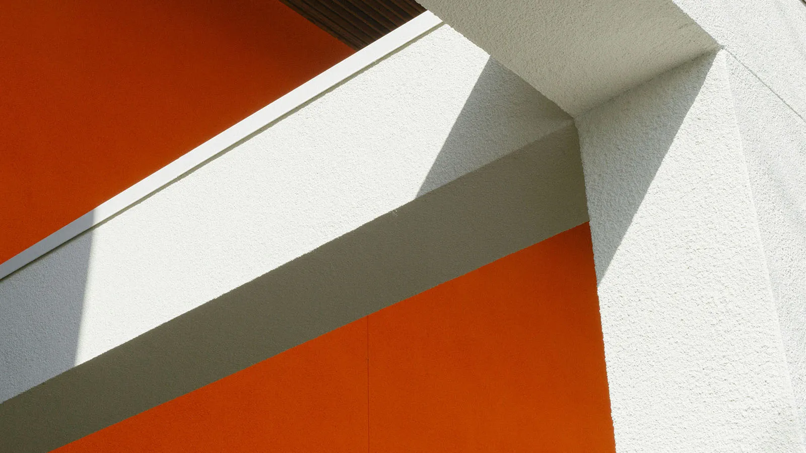 Abstract view of a modern building featuring white geometric beams, orange walls and diagonal shadows.