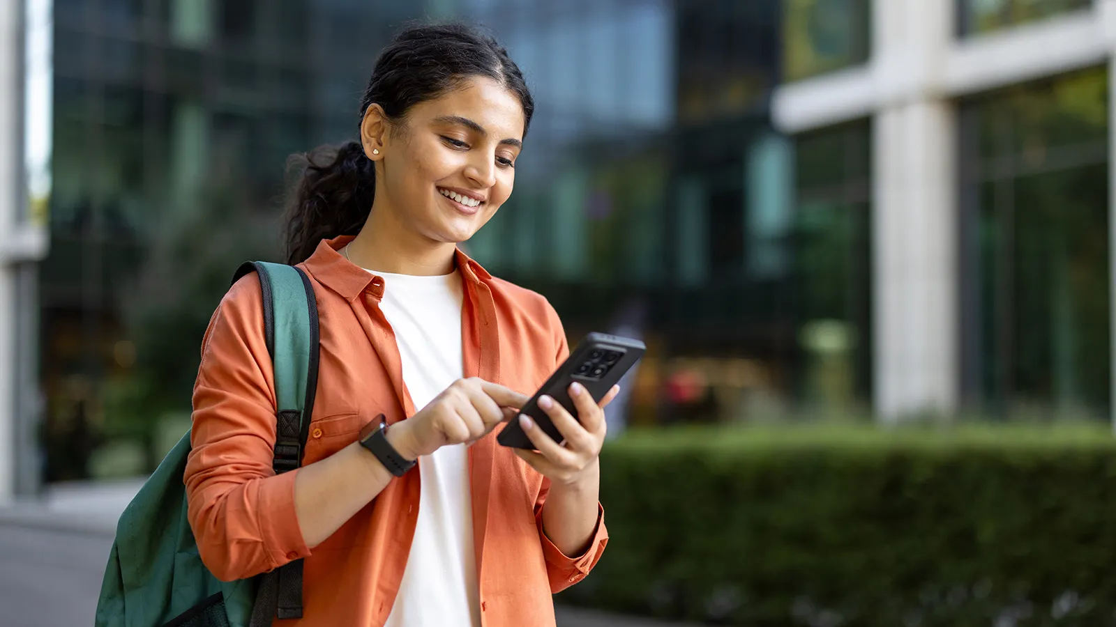 A female student in an orange shirt smiles at her mobile phone.
