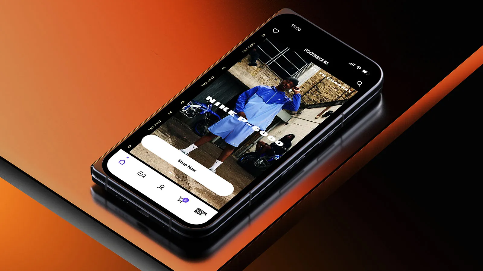 A phone displaying the Footasylum app on an orange and black background.