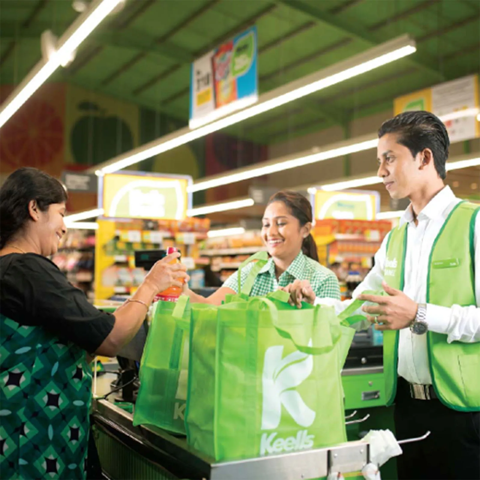 Two Keells' employees serves a female customer, packing her shopping in branded bags.