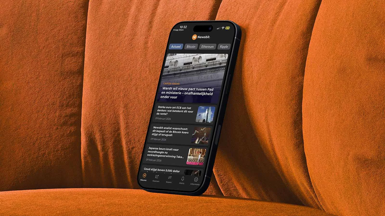 A mobile phone showing the Newsbit app rests on an orange sofa.