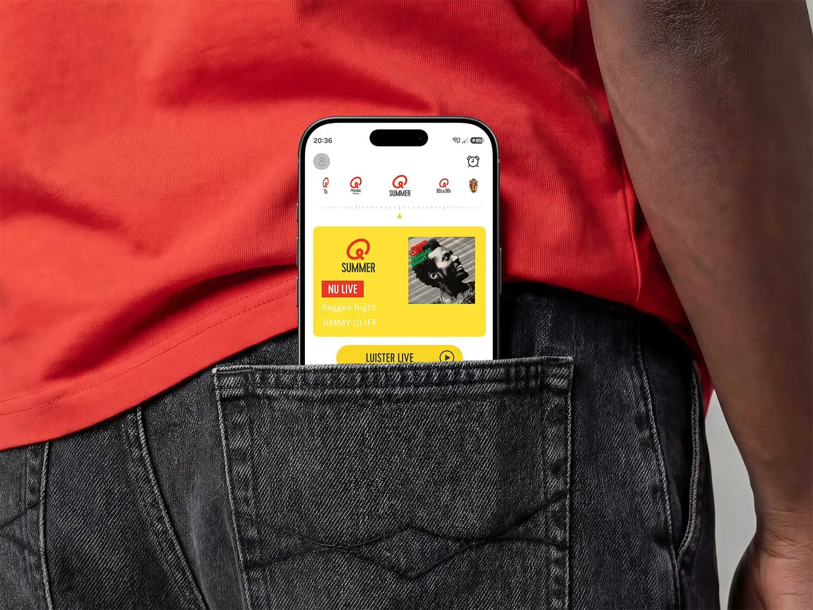 A phone displaying the Qmusic app peeks out of the back pocket of a pair of black jeans.
