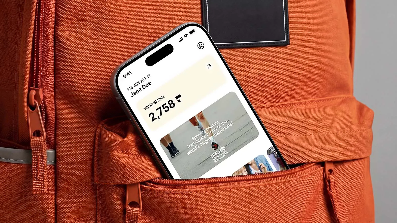 A phone displaying the Spenn app peeks out of an orange bag.