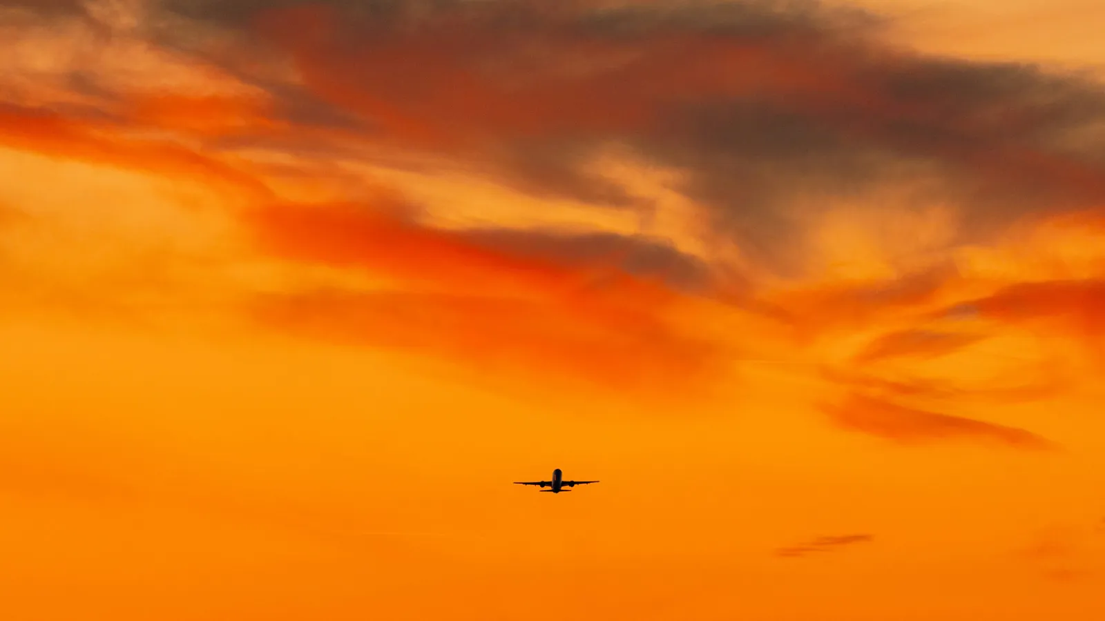 A silhouette of an airplane against an orange sky