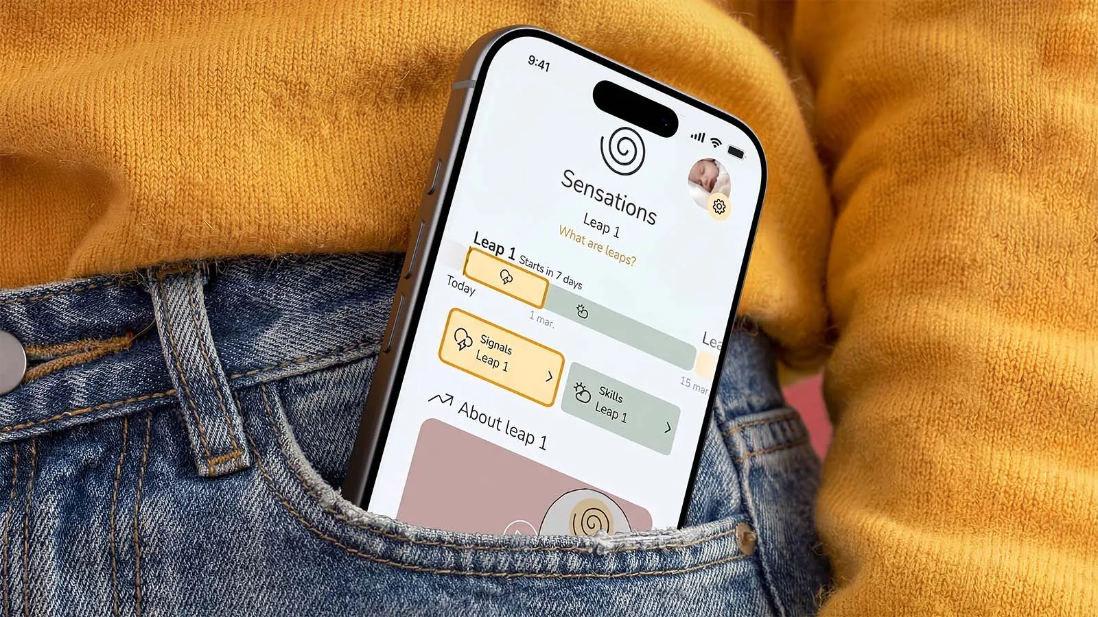 The Wonder Weeks app displayed on a smartphone tucked into the pocket of blue jeans, showing the Leap 1 development screen.