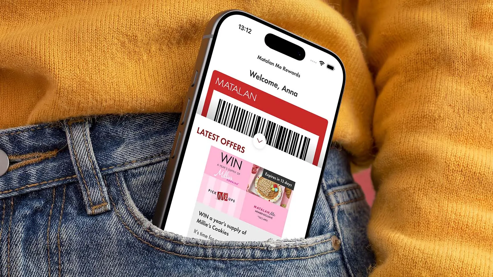A smartphone showing the Matalan shopping app peeks from a mustard-yellow sweater tucked into blue jeans, displaying offers in a casual, cozy fashion setting.